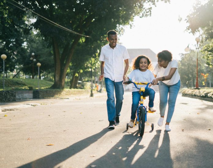 pexels-photo-1128318 man standing beside his wife teaching their child how to ride bicycle