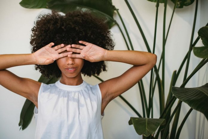 pexels-photo-5255560 black woman covering face with hands standing near potted plant